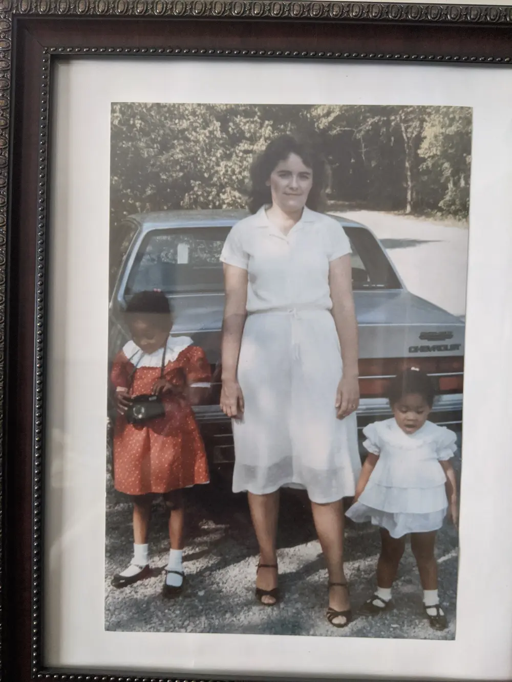 A framed family photograph of an adult and two young children beside a car