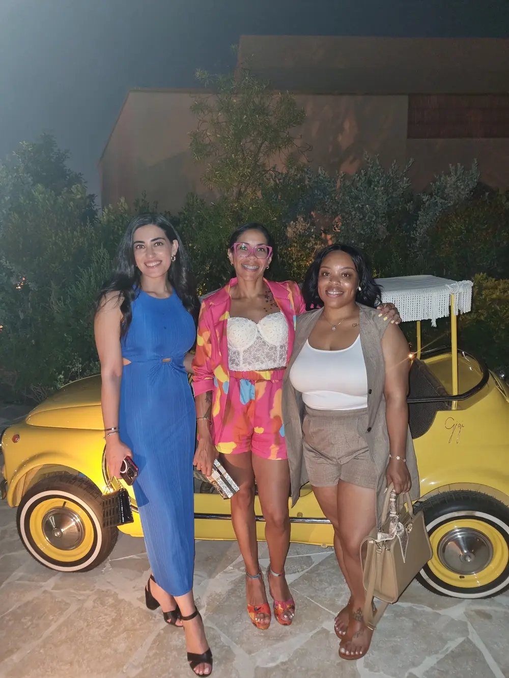 Lisa with two friends beside a yellow car on an evening out